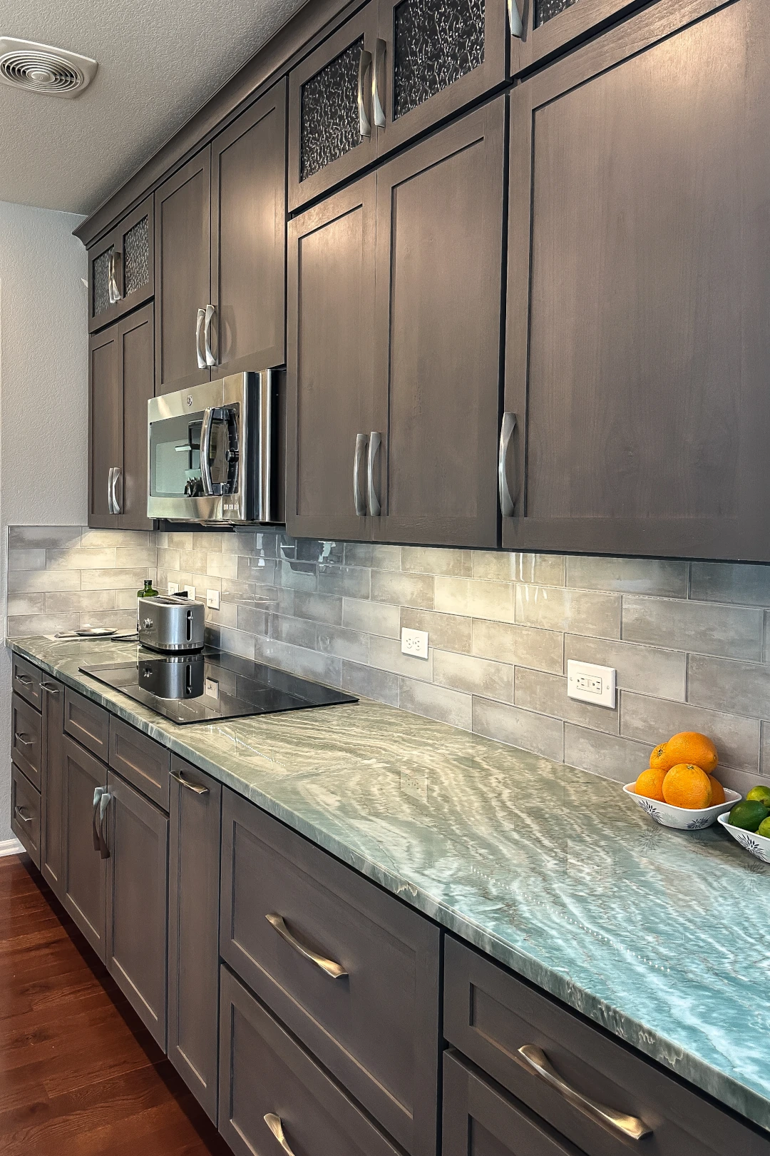 Kitchens 2 Modern kitchen with gray shaker-style cabinets, stainless steel microwave, stone countertop, and subway tile backsplash.