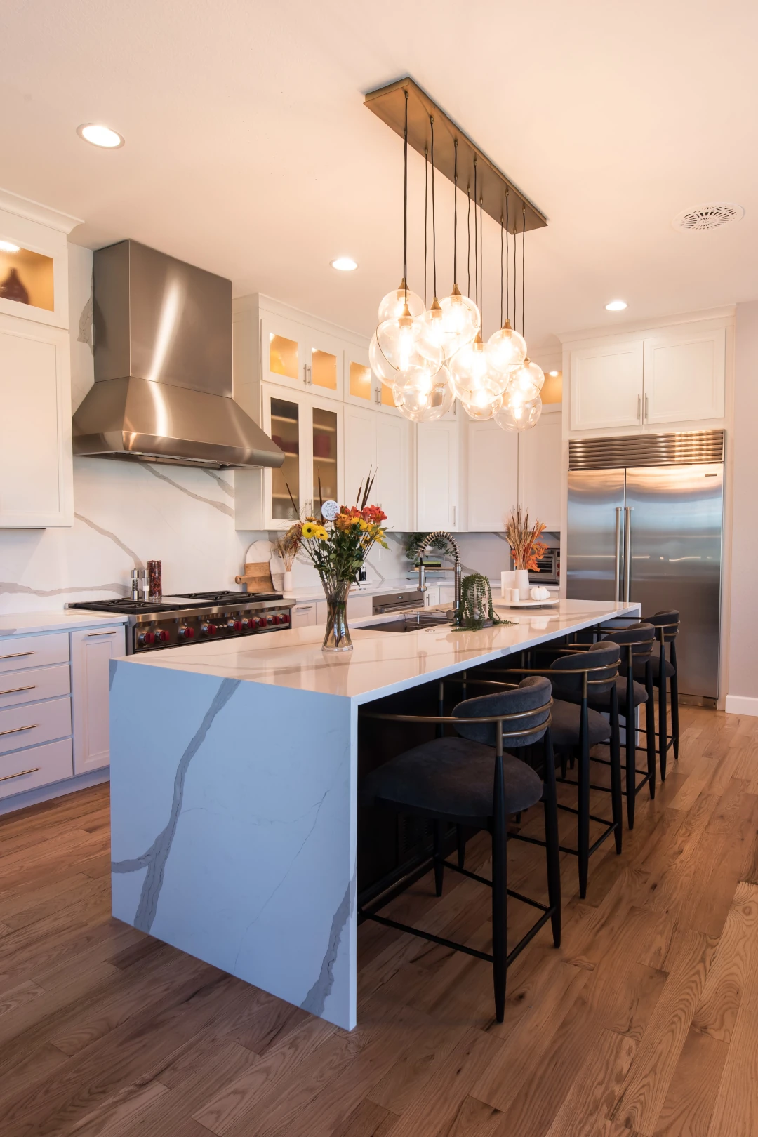 Kitchens 1 Modern kitchen with white cabinets, stainless steel appliances, quartz waterfall island, and globe pendant lighting in a Denver home remodel.