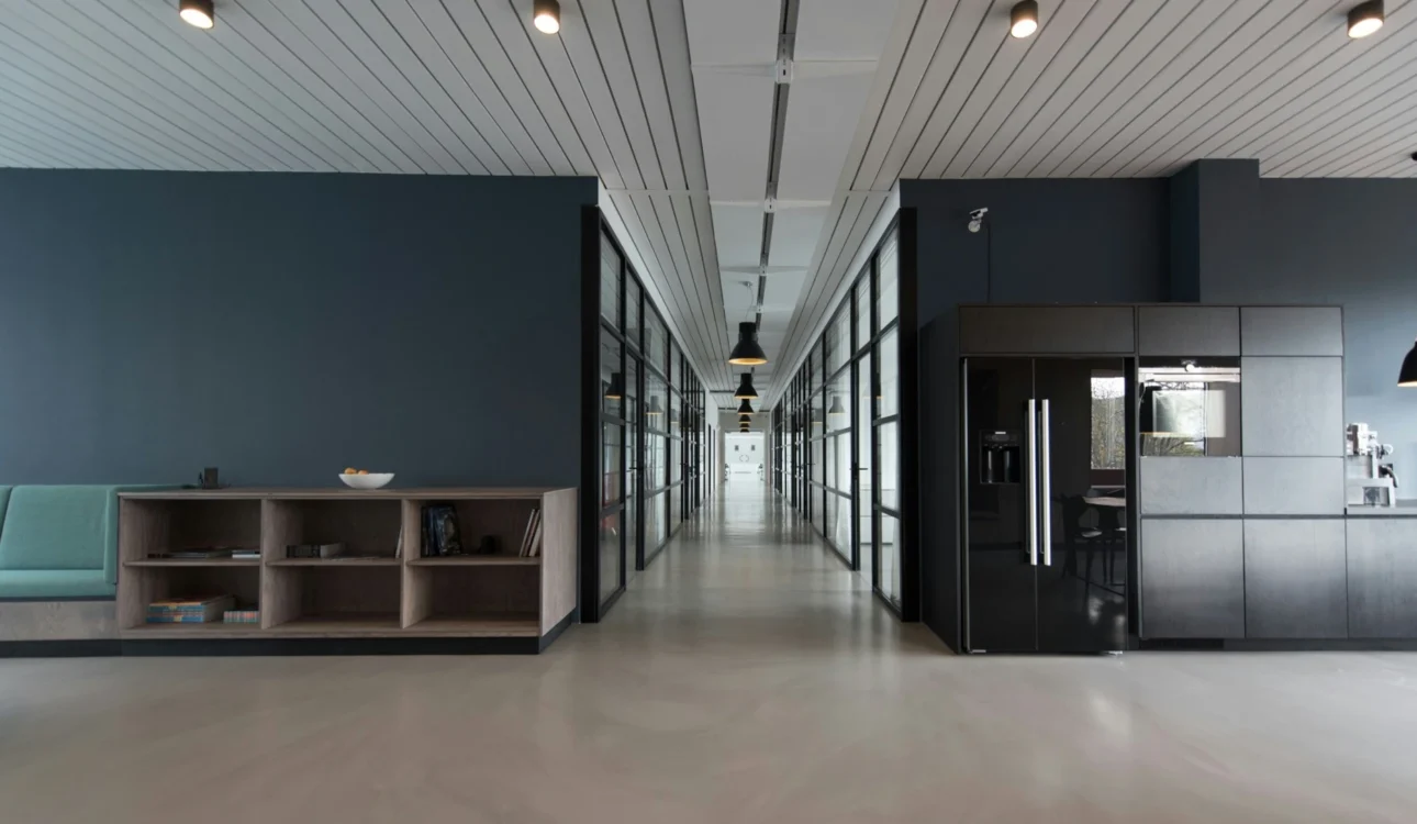 Contemporary office hallway with glass partitions, built-in cabinetry, lounge seating, and dark wood storage units.