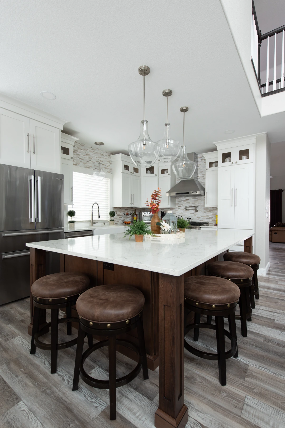 Home 1 Contemporary white kitchen featuring stainless steel appliances, a dark wood island with marble countertop, and elegant glass pendant lighting.