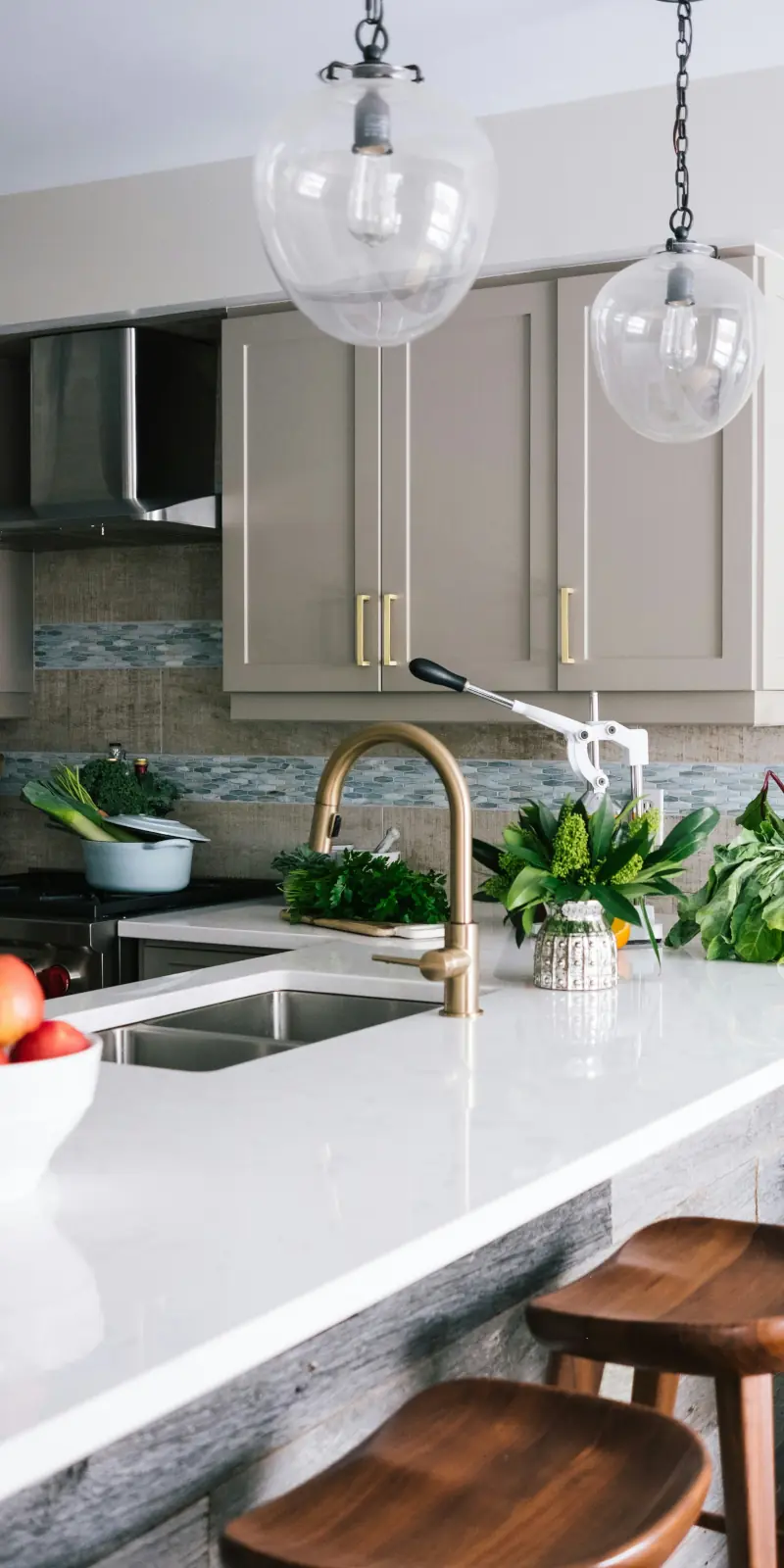 Light-colored kitchen with a brass faucet, white quartz counters, and fresh kitchen greenery.