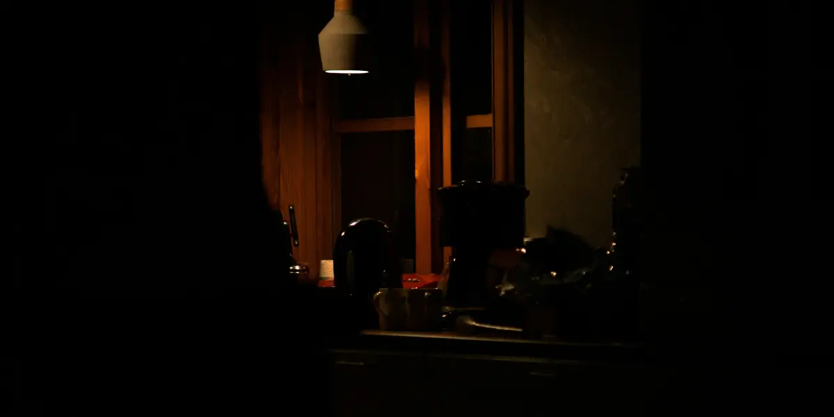 A warm, dimly lit kitchen with wood cabinetry and stainless steel appliances at night.