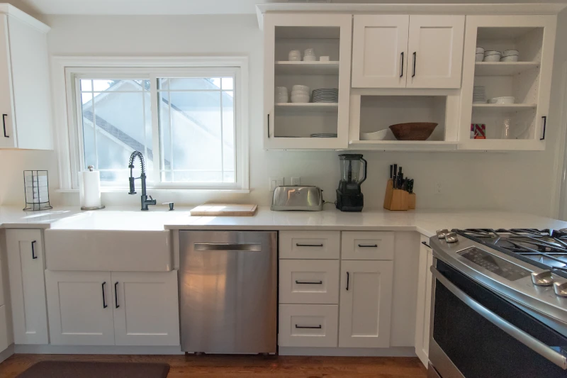 Modern white shaker kitchen with farmhouse sink, stainless steel appliances, and open shelving, featured in our kitchen bathroom remodeling process Denver project.