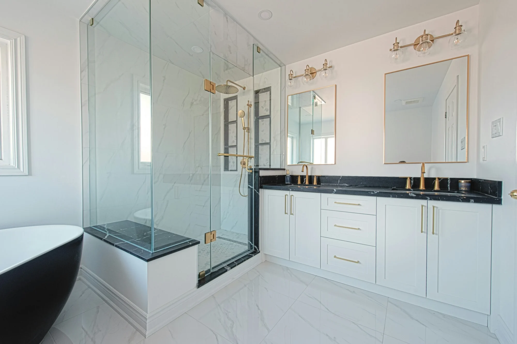White double vanity bathroom with glass shower and brass fixtures