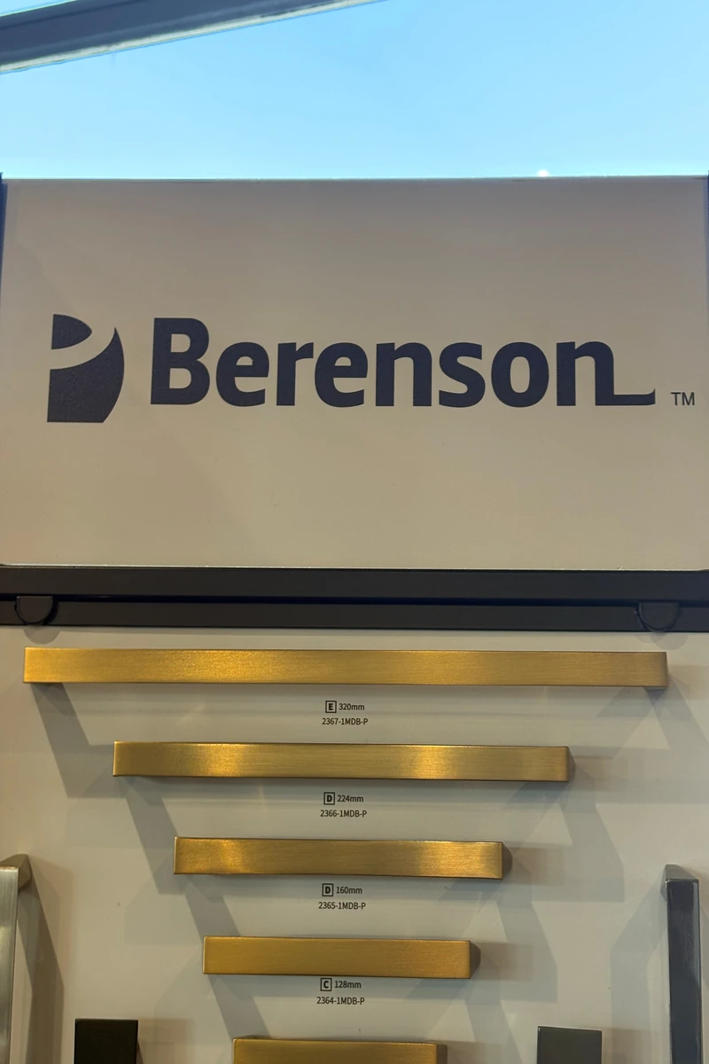 Berenson cabinet hardware display showing gold bar pulls in multiple sizes mounted on a showroom sample board.