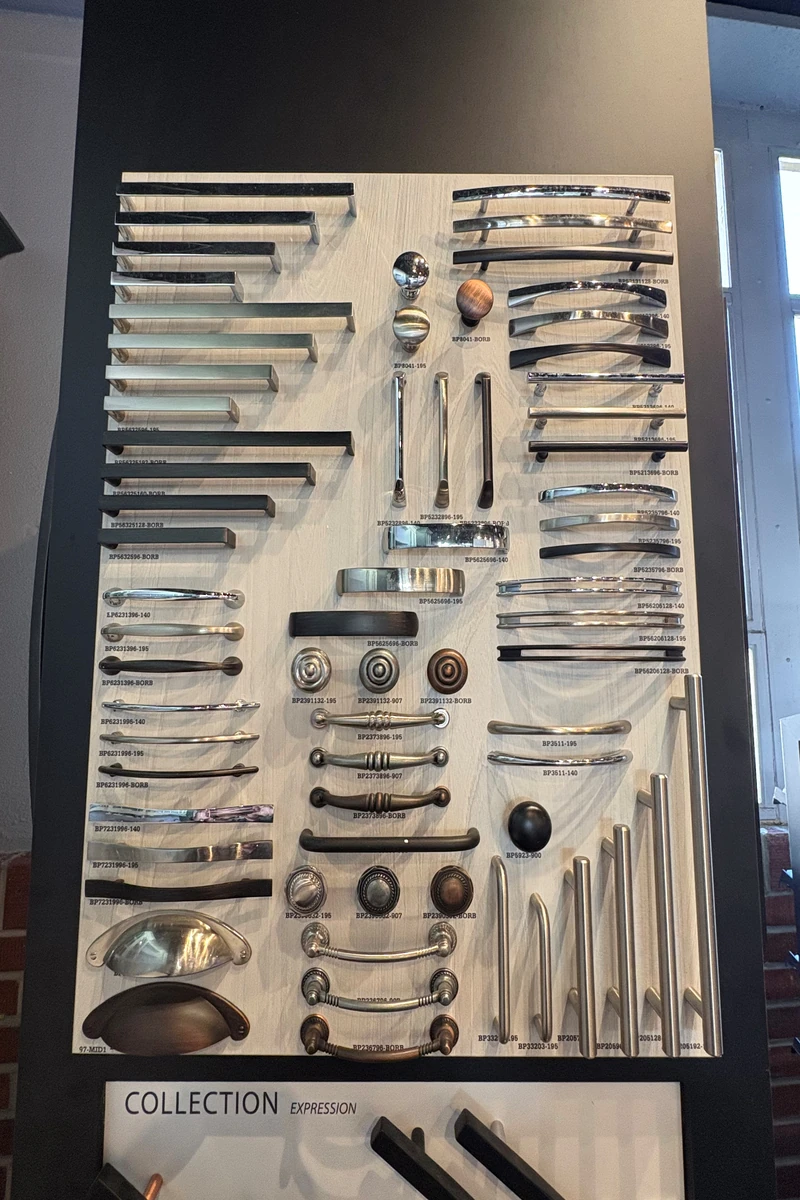 Cabinet hardware pulls and handles displaying kitchen design trends on a showroom board, with chrome, black, brushed metal, and wood finish options.