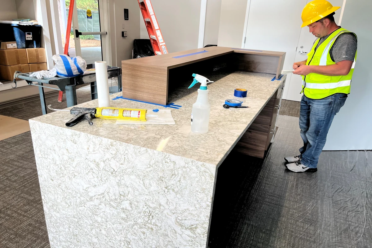 Your Denver Kitchen Remodel Guide: Custom Work, Fast Timelines, and a Kitchen You Will Actually Love 8 Technician installing a custom commercial reception desk with stone countertop in an office building.