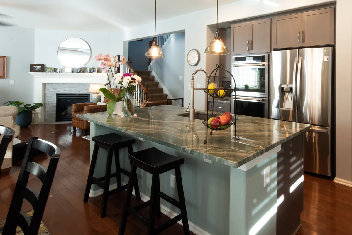 Open kitchen with granite island, pendant lighting, stainless appliances, bar seating, and living room fireplace in the background.