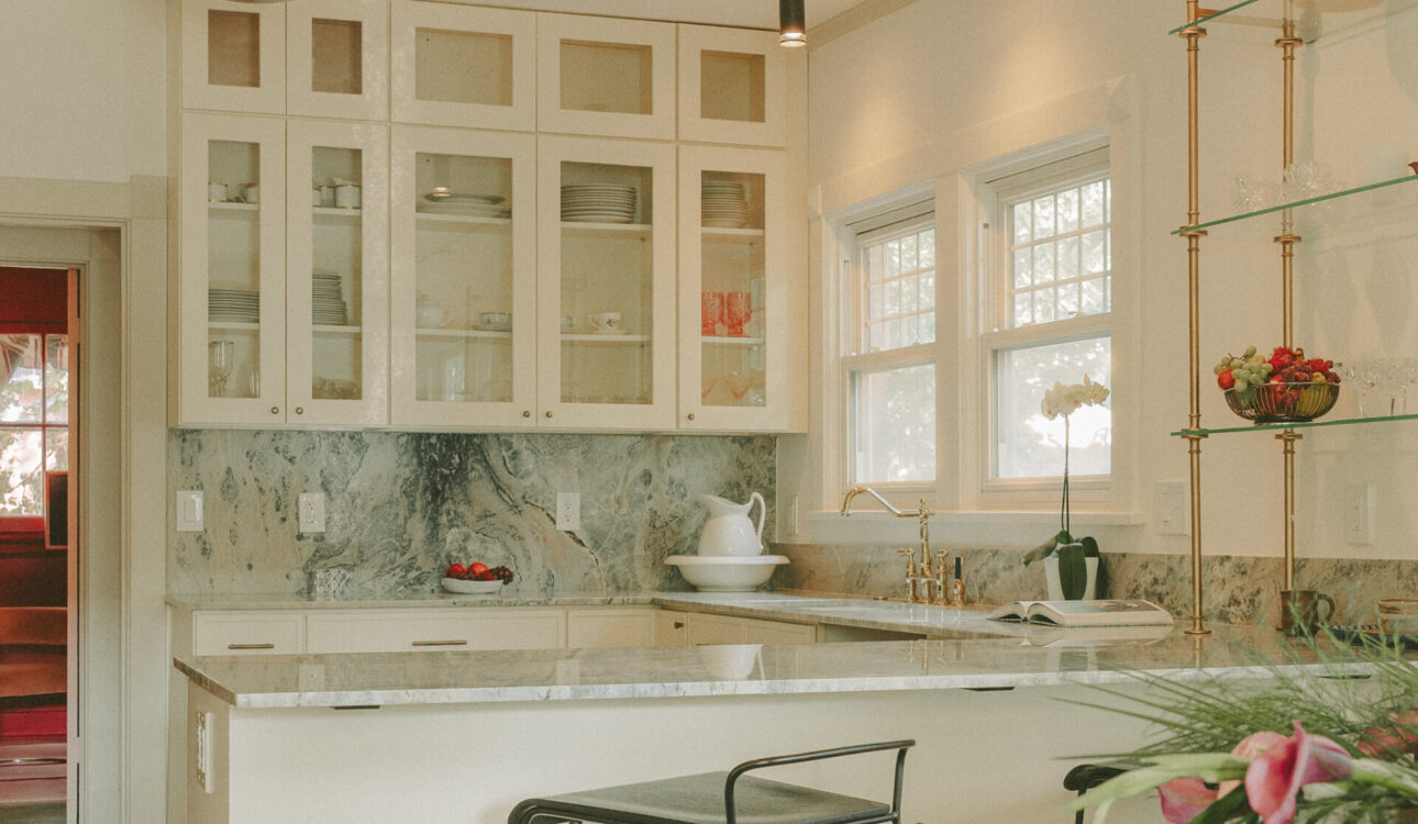 Custom kitchen with glass-front upper cabinets, marble backsplash, quartz island, brass fixtures, and open shelving.