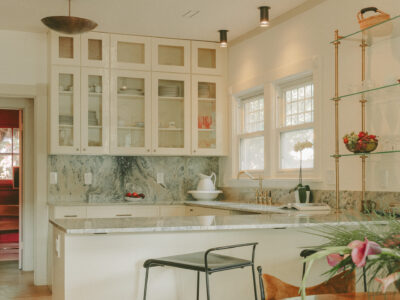 Custom kitchen with glass-front upper cabinets, marble backsplash, quartz island, brass fixtures, and open shelving.