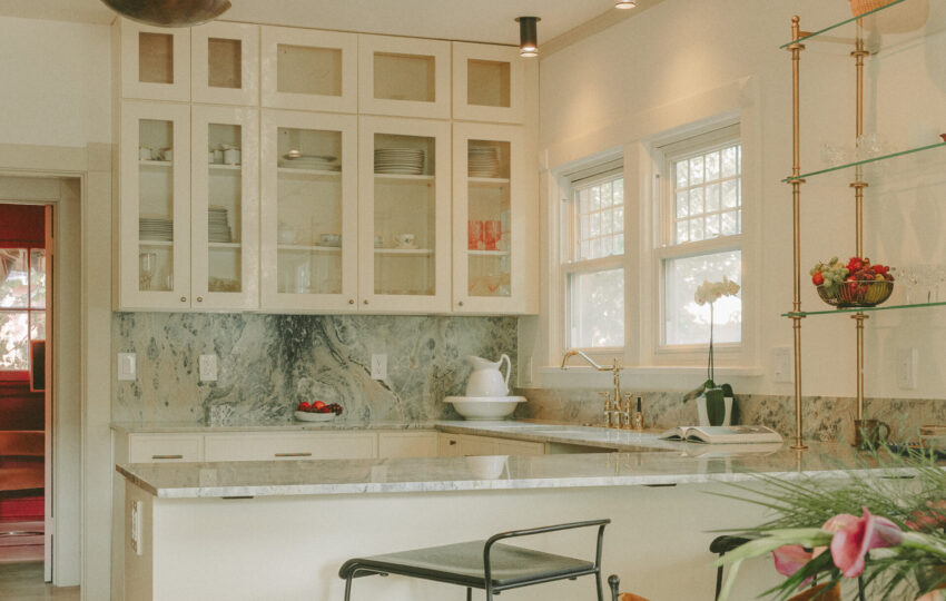 Custom kitchen with glass-front upper cabinets, marble backsplash, quartz island, brass fixtures, and open shelving.