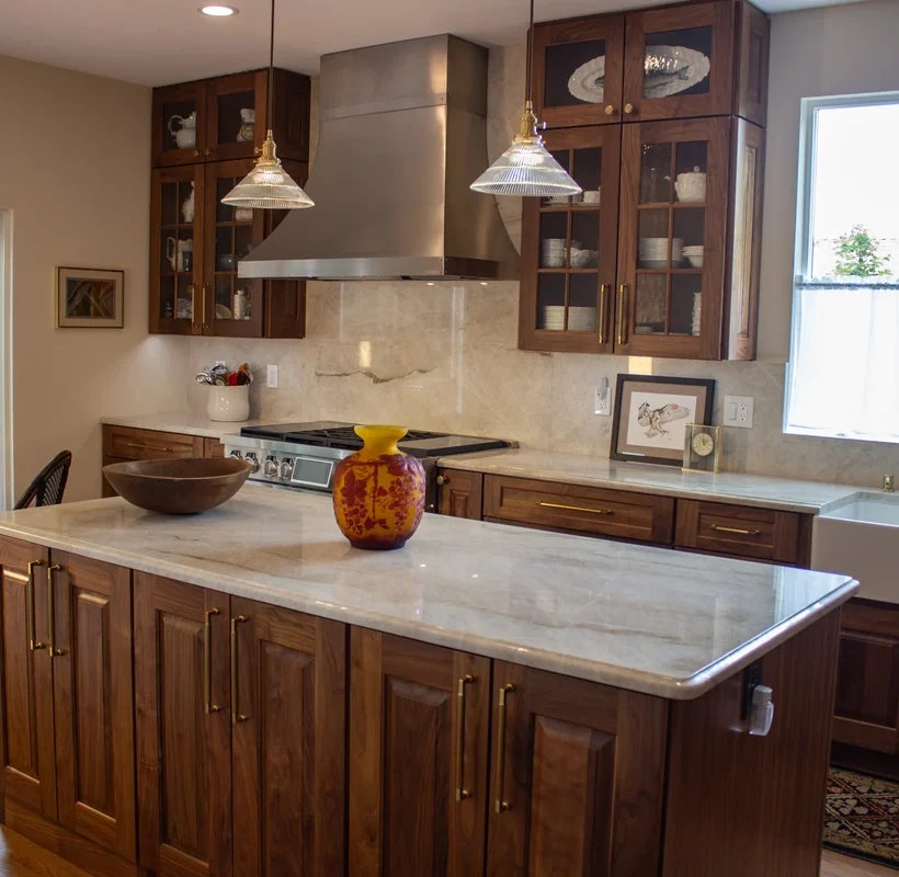 Light stone countertop on a kitchen island with dark wood cabinets and pendant lighting