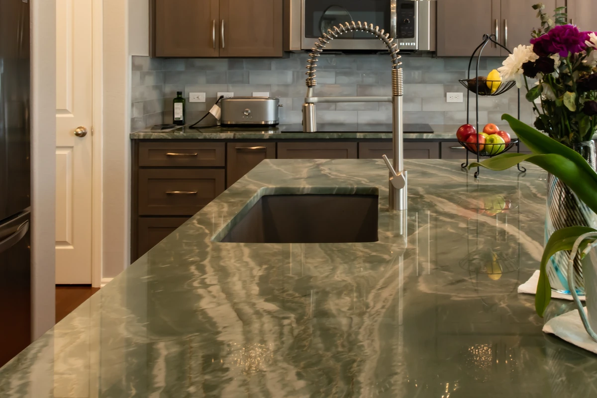 Leathered Quartzite Countertops: Cleaning, Sealing, and What to Check Before Buying 4 Green veined stone countertop surrounding a rectangular undermount sink with a tall spring faucet
